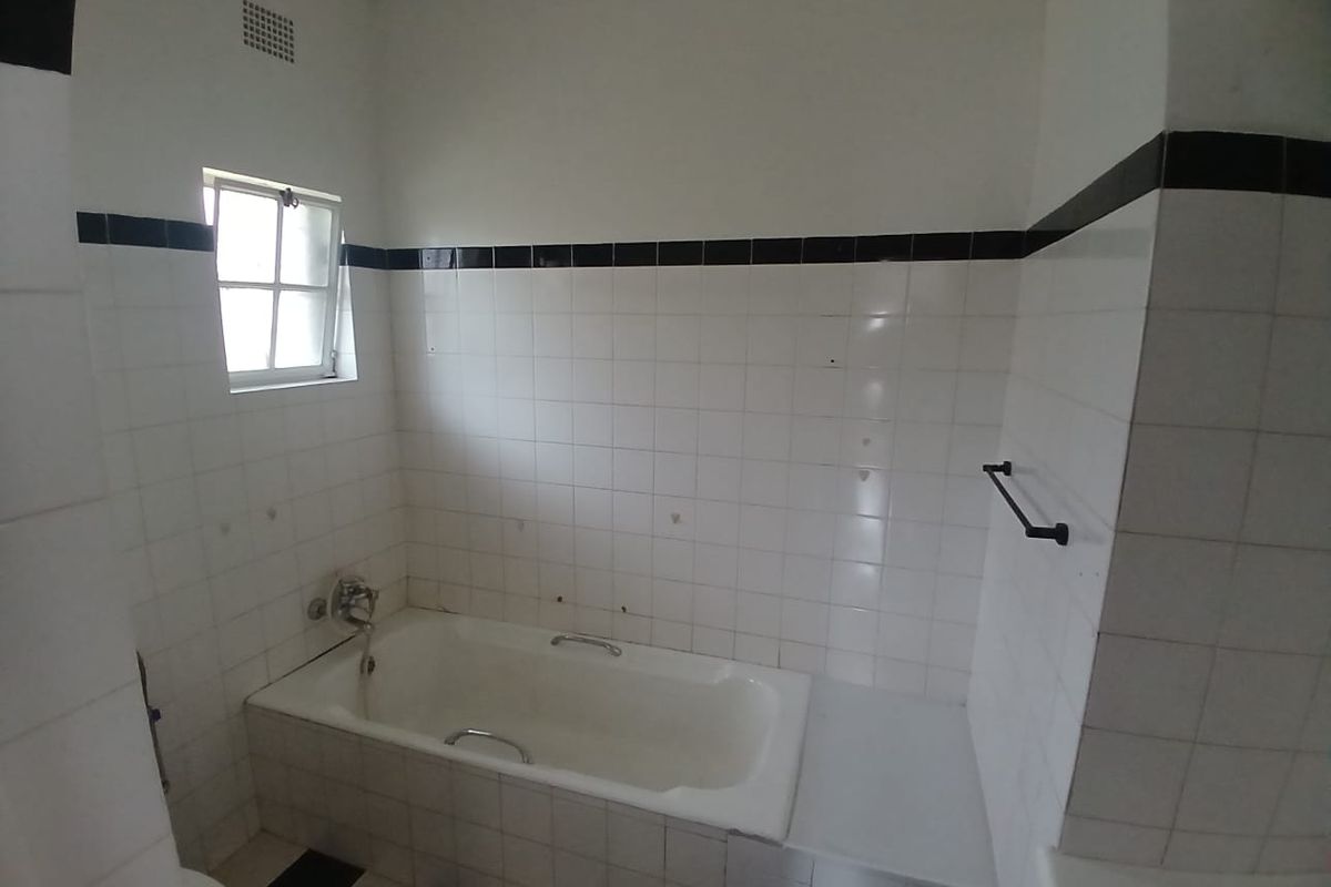 A dated bathroom featuring a built-in bathtub with a black and white tiled surround and matching floor tiles.