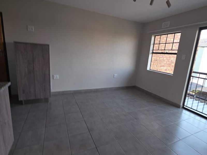 An empty, tiled living area featuring a ceiling spotlight track, large window with security bars, and a sliding door leading to an outdoor space.