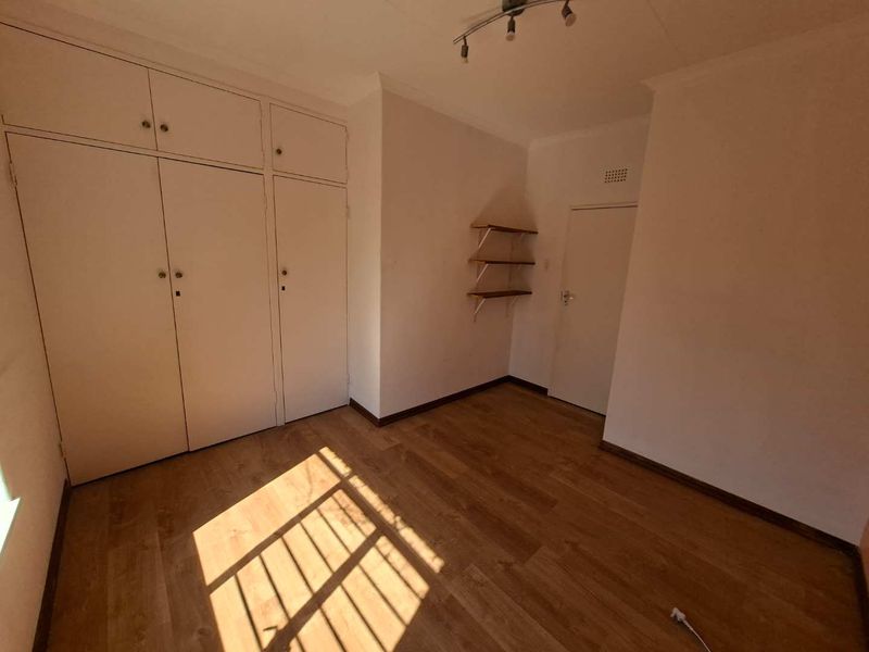 An empty bedroom featuring laminate flooring, built-in cupboards, and wall-mounted shelving, offering a blank canvas for personalization.