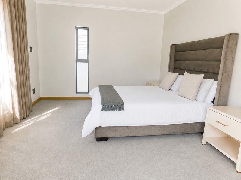 A well-maintained bedroom featuring neutral carpet flooring, clean wall finishes, and a vertical window allowing natural light.