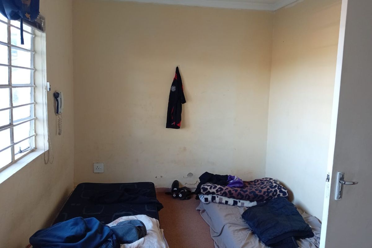 A compact bedroom featuring a window with security bars and standard interior finishes, requiring cosmetic updates to improve the overall condition.