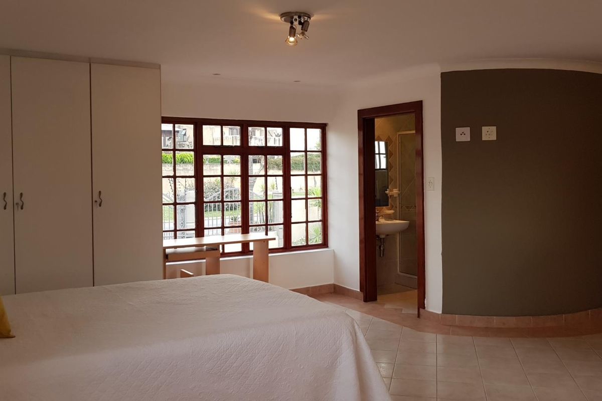 A spacious bedroom featuring built-in cupboards, tiled flooring, and an en-suite bathroom with a view through large paneled windows.