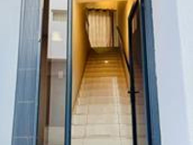 A modern entrance featuring a tiled staircase with a metal handrail, accessed through a contemporary glass-paneled door.