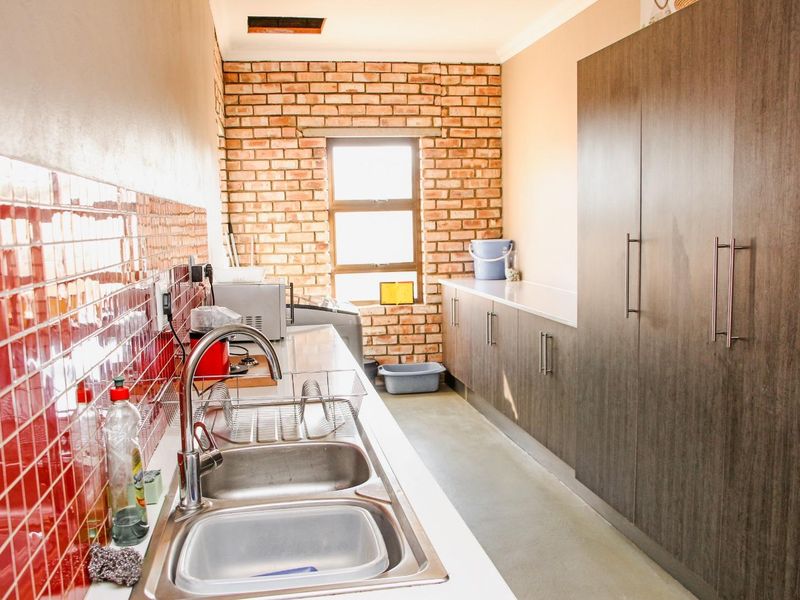 A functional scullery featuring a double stainless steel sink, ample built-in cabinetry, and an exposed brick feature wall.
