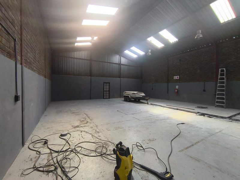 Spacious industrial utility area featuring high ceilings with skylights, exposed brick walls, and durable concrete flooring, suitable for storage or workshop use.