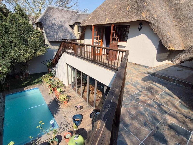 Rear exterior view featuring a swimming pool, a tiled patio area, and a raised balcony with wooden railings under a traditional thatched roof.