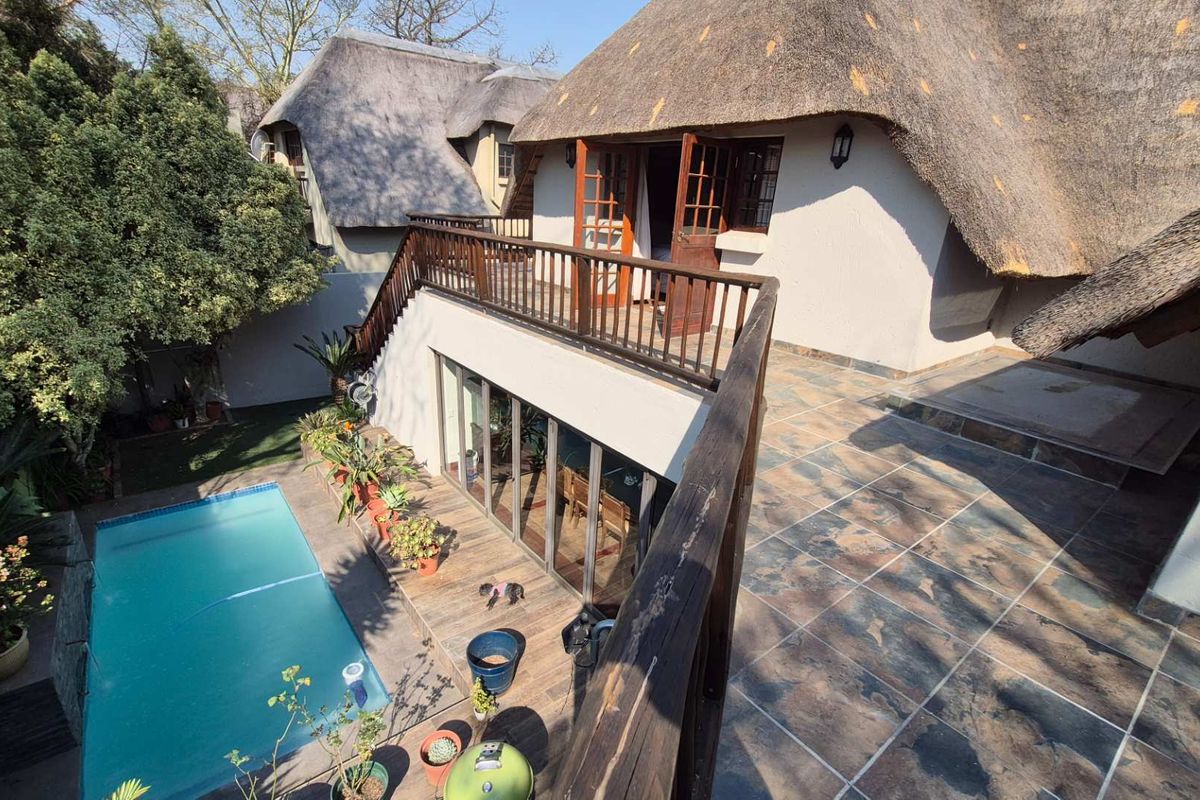 Rear exterior view featuring a swimming pool, a tiled patio area, and a raised balcony with wooden railings under a traditional thatched roof.