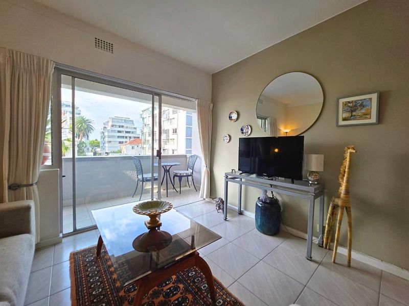 A bright living room featuring tiled flooring and a large sliding glass door that opens onto a private balcony with urban views.