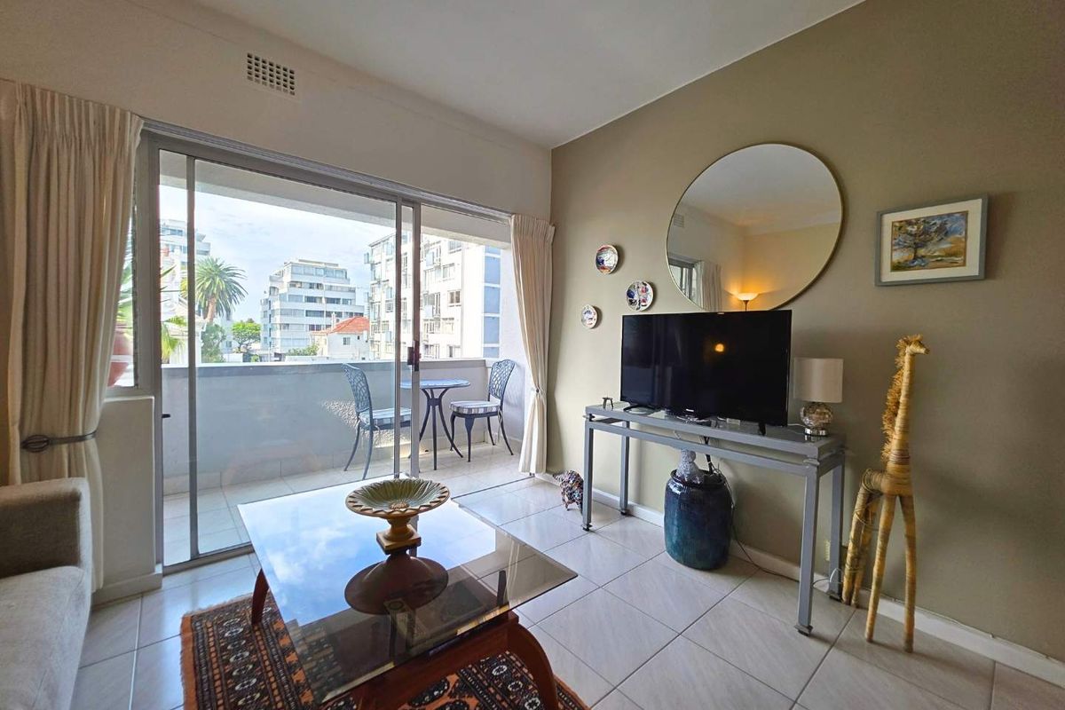 A bright living room featuring tiled flooring and a large sliding glass door that opens onto a private balcony with urban views.
