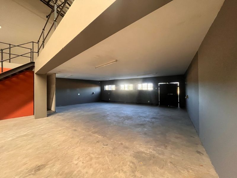 Spacious industrial utility area featuring concrete flooring, a mezzanine level with metal staircase, and secure window access, suitable for storage or workshop use.