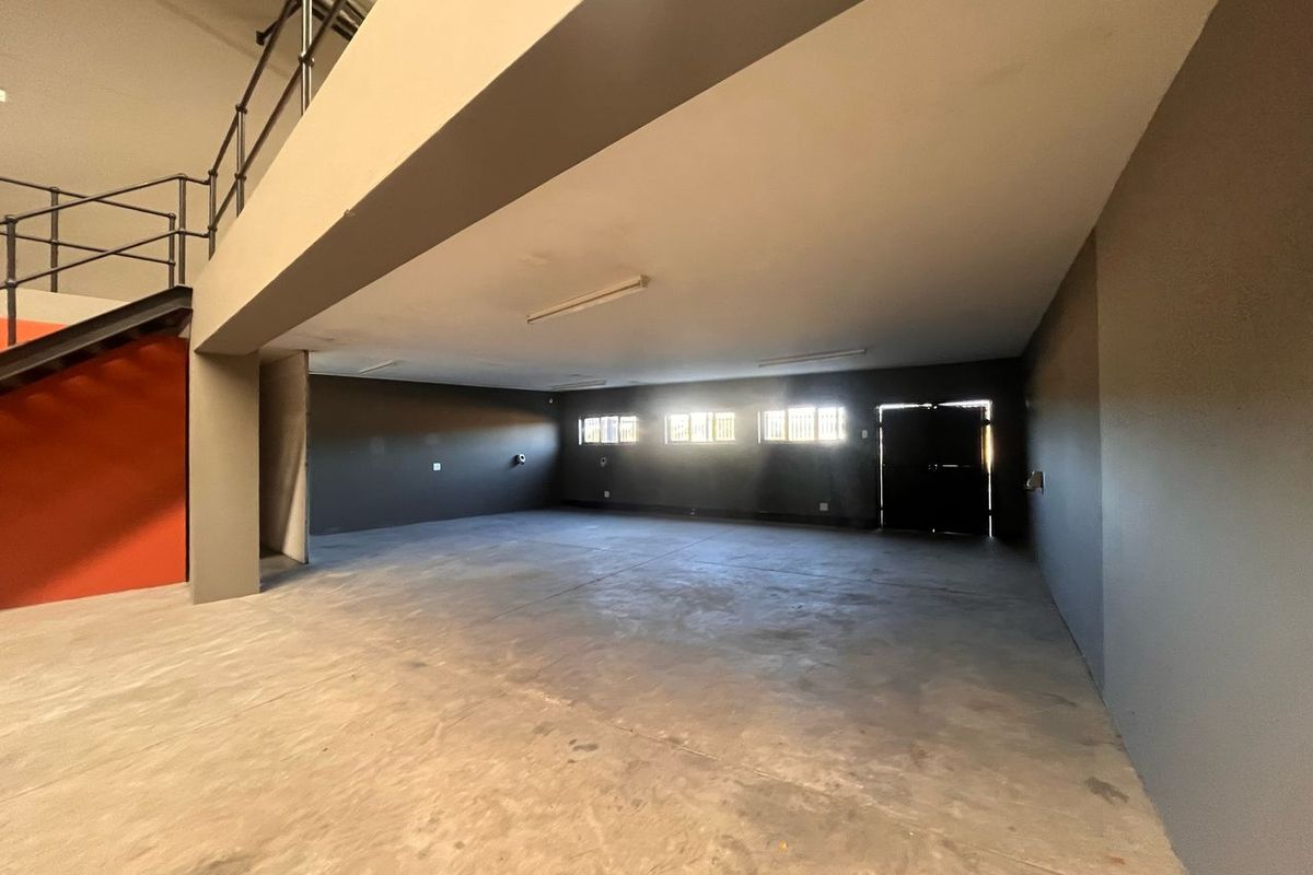Spacious industrial utility area featuring concrete flooring, a mezzanine level with metal staircase, and secure window access, suitable for storage or workshop use.