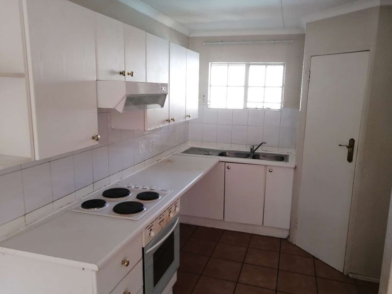 A functional kitchen featuring white built-in cabinetry, an electric hob, oven, extractor fan, and a double bowl sink with tiled splashbacks.