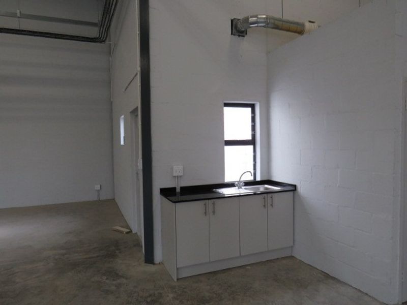 A functional kitchenette area within an industrial space, featuring built-in cabinetry, a sink, and exposed ventilation ducting against a painted block wall.
