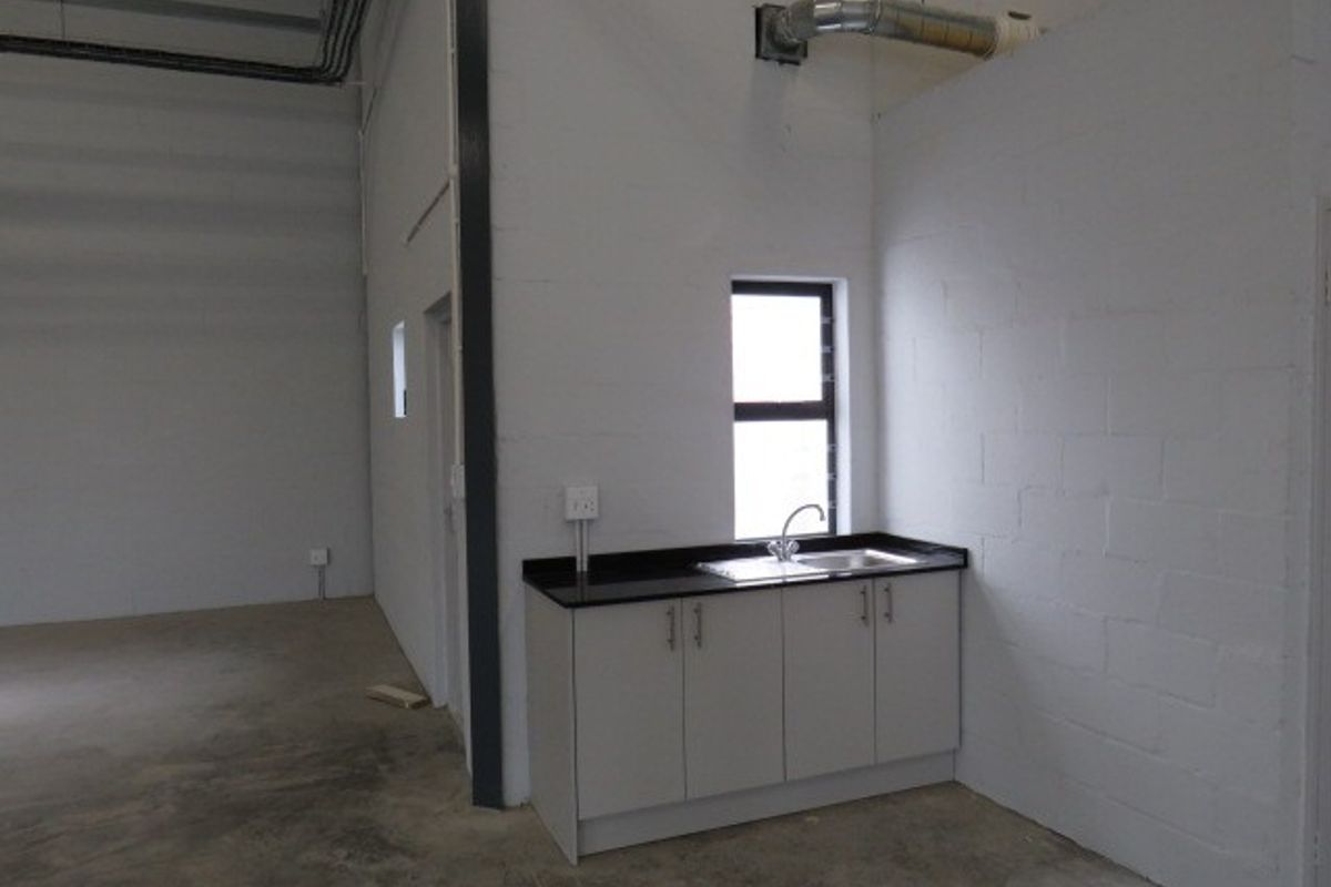 A functional kitchenette area within an industrial space, featuring built-in cabinetry, a sink, and exposed ventilation ducting against a painted block wall.