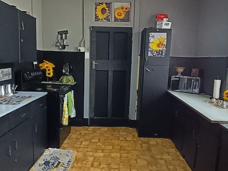 A functional kitchen featuring dark cabinetry, laminate countertops, a stainless steel sink, and a freestanding stove, with tiled flooring and natural light.