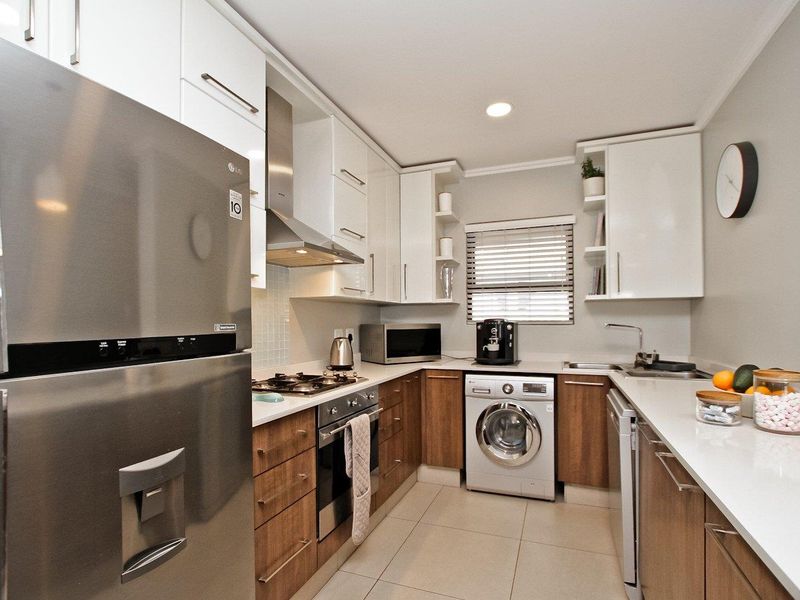 Modern kitchen featuring sleek white and wood-tone cabinetry, stone countertops, integrated appliances, and high-quality finishes in a well-organized layout.