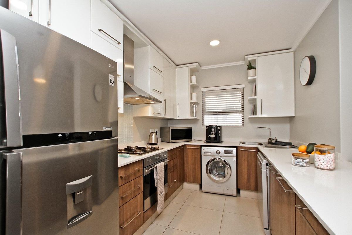 Modern kitchen featuring sleek white and wood-tone cabinetry, stone countertops, integrated appliances, and high-quality finishes in a well-organized layout.
