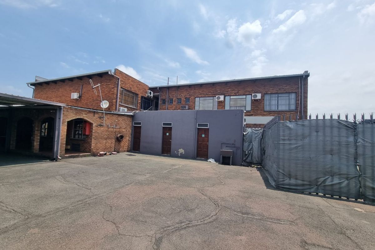 Rear exterior view of a mixed-use property featuring a brick facade, paved driveway, security fencing, and multiple access points.