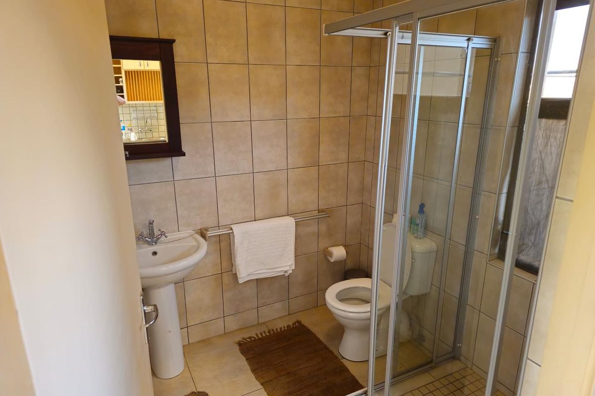 A functional bathroom featuring a pedestal basin, a toilet, and a glass-enclosed shower with neutral wall and floor tiling.