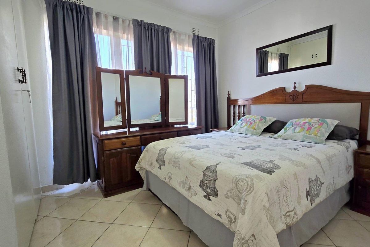 A well-lit bedroom featuring tiled flooring, built-in cupboards, and large windows with curtain tracks.
