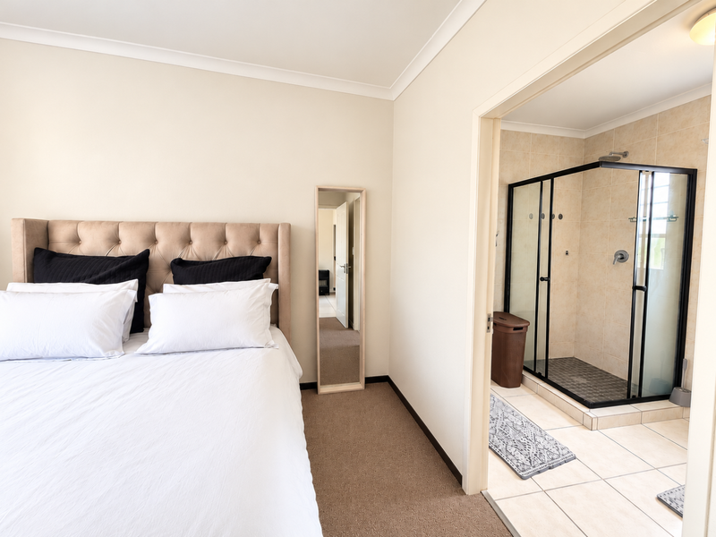 A well-maintained bedroom featuring neutral carpeting and an adjoining en-suite bathroom with a modern glass-enclosed shower and tiled finishes.