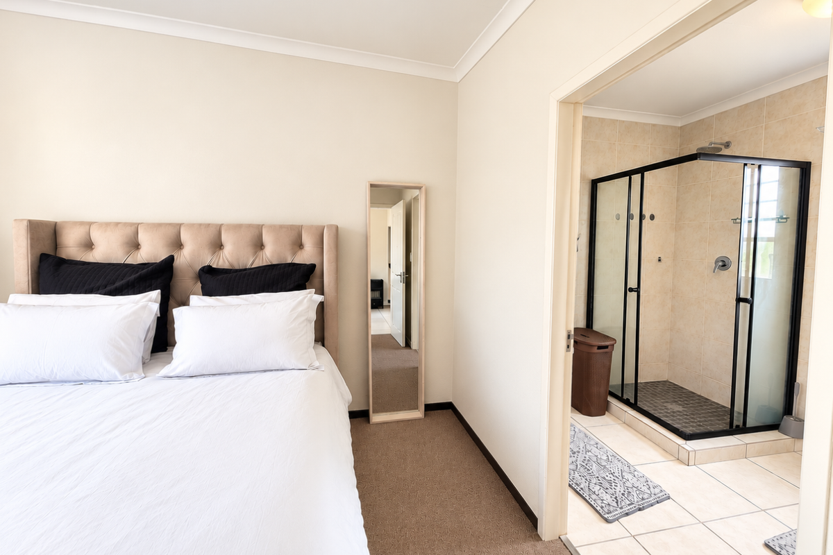 A well-maintained bedroom featuring neutral carpeting and an adjoining en-suite bathroom with a modern glass-enclosed shower and tiled finishes.