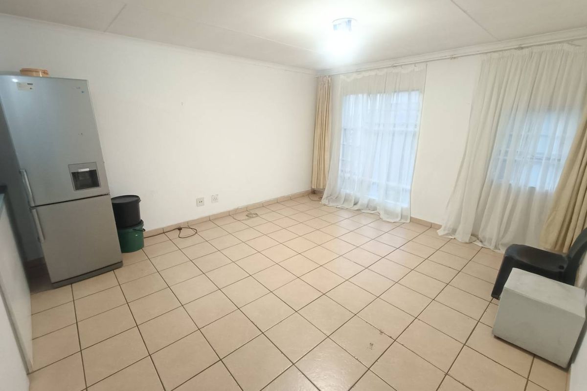 A spacious, empty living area featuring neutral ceramic floor tiles and large windows with installed curtain tracks, offering a blank canvas for interior design.