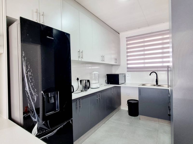 Modern galley-style kitchen featuring sleek two-tone cabinetry, tiled backsplash, double sink with mixer tap, and neutral floor tiles.