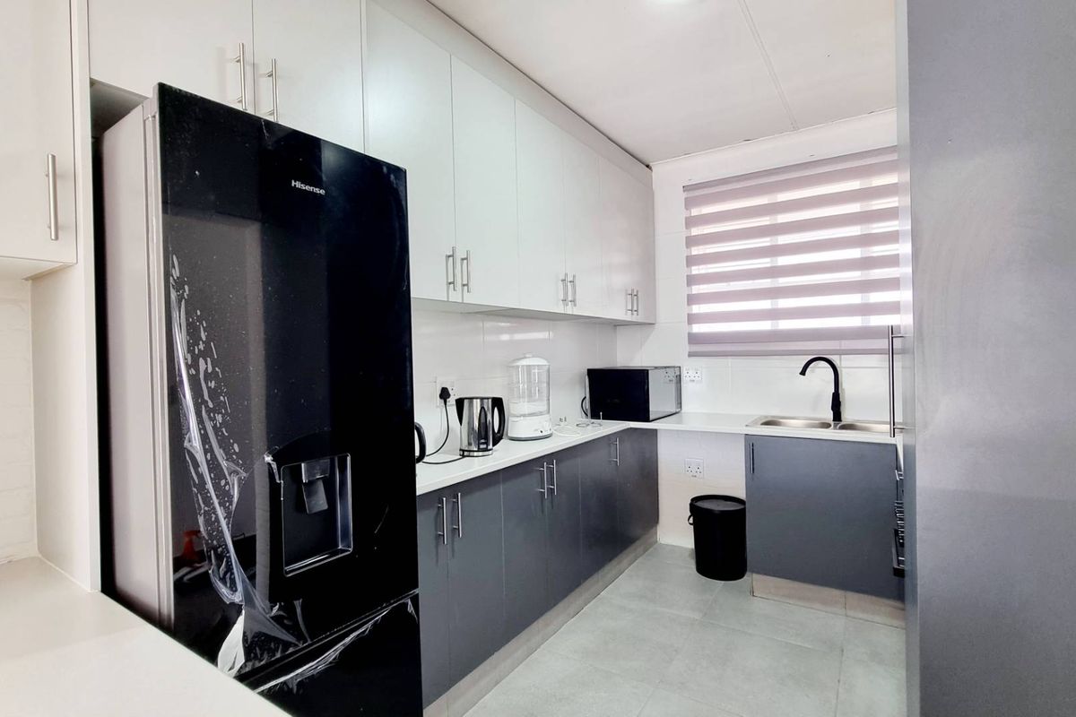 Modern galley-style kitchen featuring sleek two-tone cabinetry, tiled backsplash, double sink with mixer tap, and neutral floor tiles.