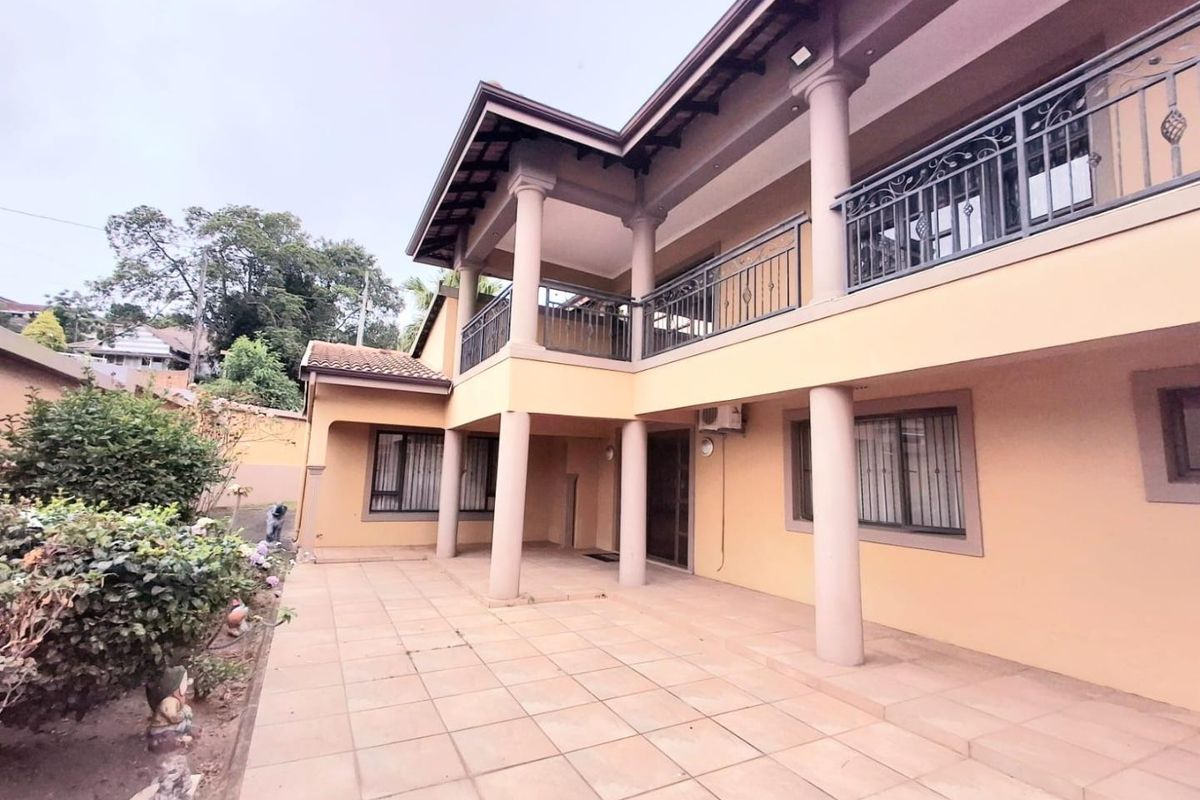 A spacious rear exterior view featuring a covered tiled patio, a second-story balcony with wrought iron railings, and structural concrete columns.