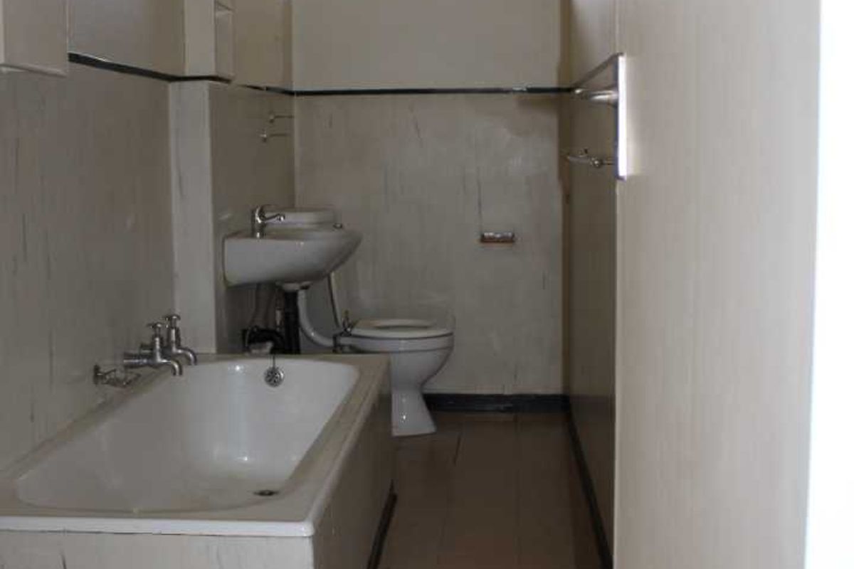 A dated bathroom featuring a standard bathtub, pedestal basin, and toilet, with original wall tiling and a sliding window for ventilation.