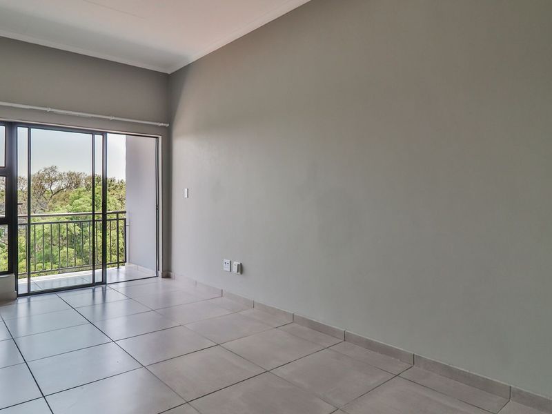 A bright, empty living area featuring neutral tiled flooring and a large sliding glass door providing direct access to a private balcony.