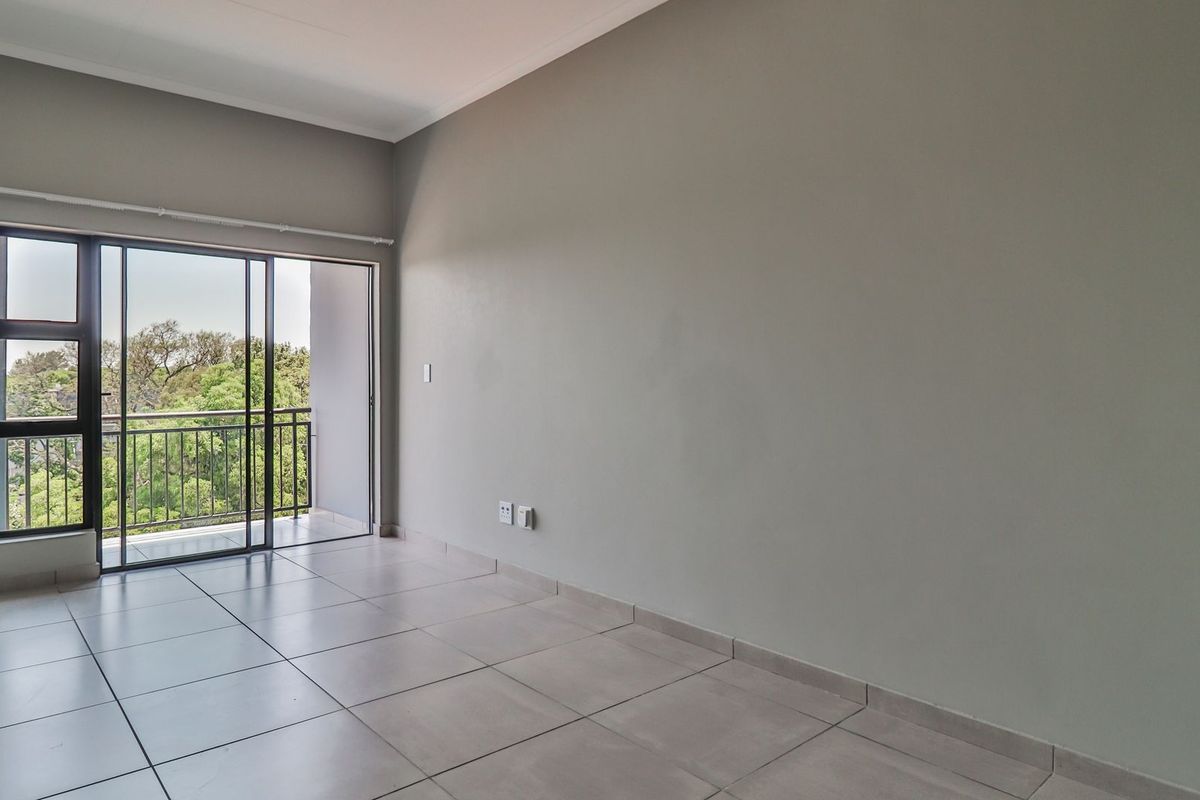 A bright, empty living area featuring neutral tiled flooring and a large sliding glass door providing direct access to a private balcony.