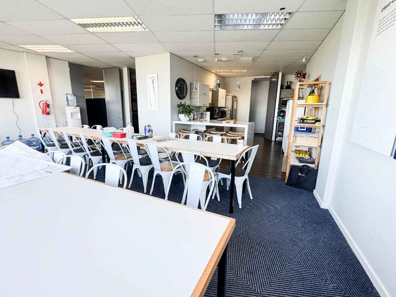 Open-plan office space featuring a kitchenette with island, suspended ceiling with recessed lighting, and carpeted flooring, suitable for collaborative work or break area.
