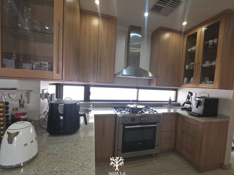 A well-maintained kitchen featuring granite countertops, stainless steel gas stove with extractor fan, and ample wooden cabinetry with glass-fronted display units.