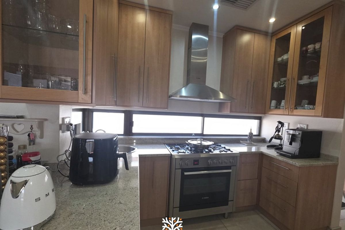 A well-maintained kitchen featuring granite countertops, stainless steel gas stove with extractor fan, and ample wooden cabinetry with glass-fronted display units.