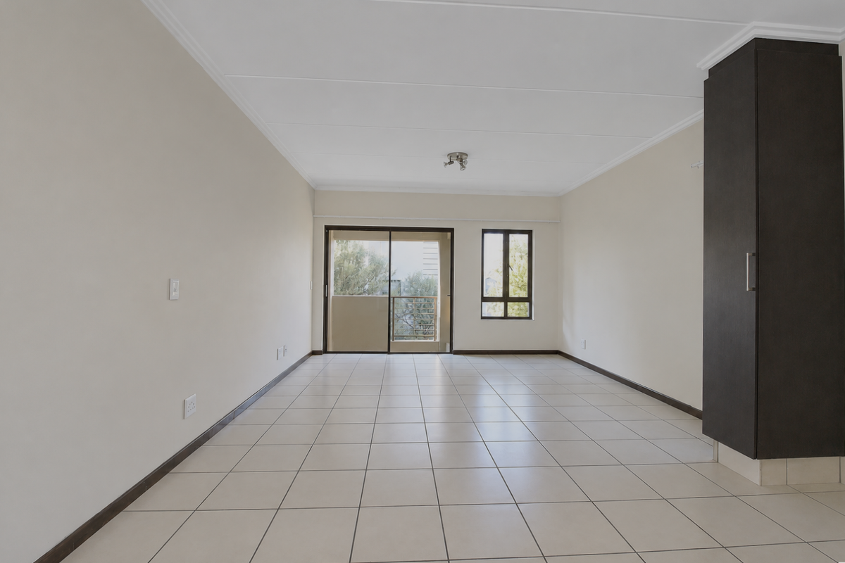 A bright, open-plan living area featuring neutral tiled flooring, built-in dark cabinetry, and access to a balcony through a sliding glass door.