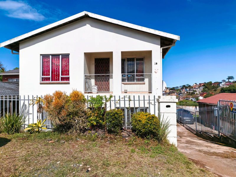 Front elevation of a detached house featuring a covered entrance porch, metal security fixtures, and a concrete driveway with perimeter fencing.