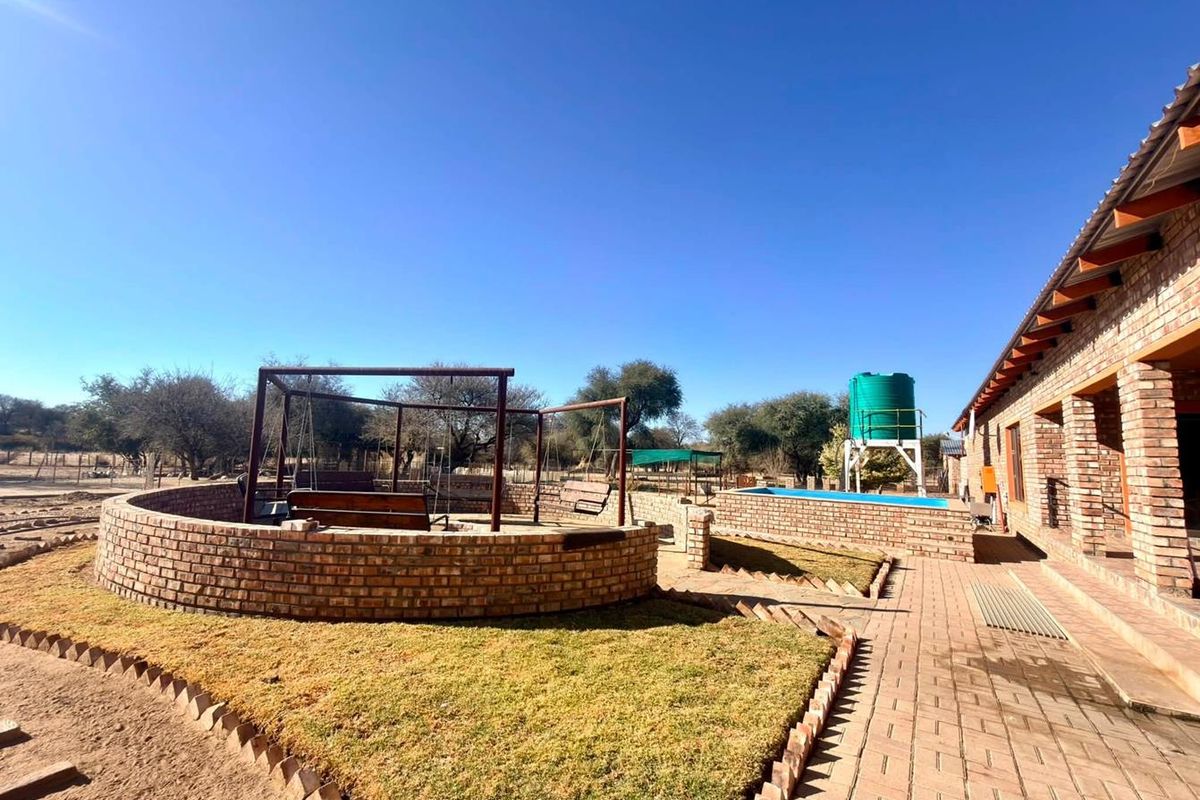 Rear exterior view of a small holding featuring a brick fire pit, paved walkway, swimming pool, and elevated water storage tank.