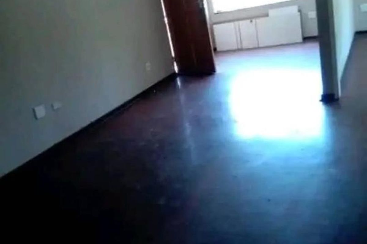An empty living area featuring dark flooring, neutral walls, and natural light from a large window.