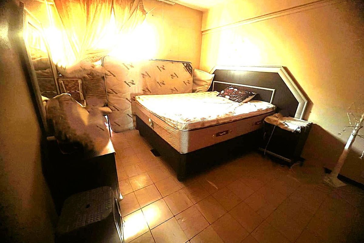 A bedroom featuring tiled flooring and a built-in headboard, currently requiring cosmetic updates to improve the overall aesthetic and finish.
