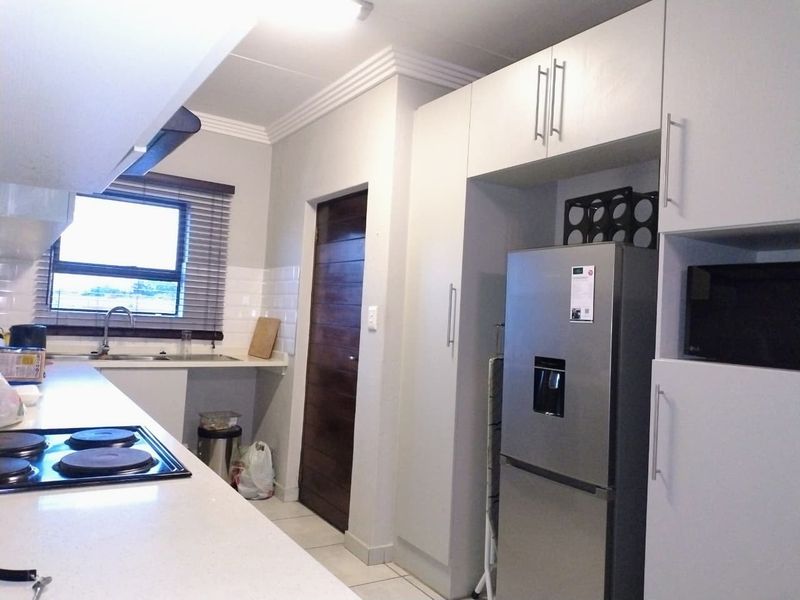 A functional kitchen featuring white built-in cabinetry, a subway tile backsplash, an electric hob, and an integrated microwave with tiled flooring.