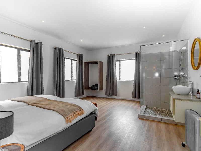 Spacious bedroom featuring modern laminate flooring, recessed lighting, and an integrated open-plan glass shower enclosure with a contemporary vessel sink.
