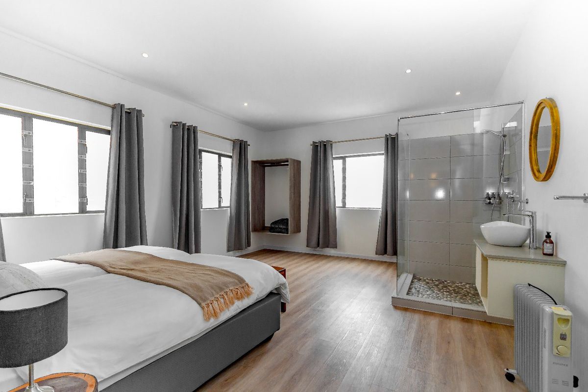 Spacious bedroom featuring modern laminate flooring, recessed lighting, and an integrated open-plan glass shower enclosure with a contemporary vessel sink.