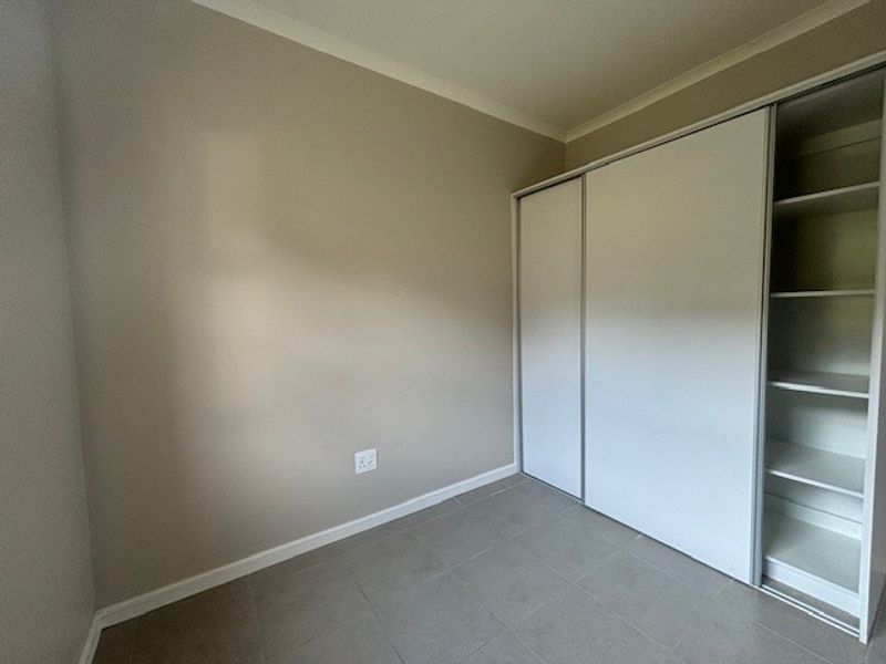 A clean, empty bedroom featuring neutral wall tones, tiled flooring, and a functional built-in sliding door wardrobe with internal shelving.