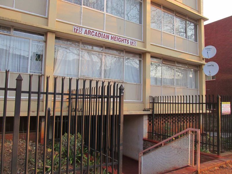 Front facade of Arcadian Heights apartment building featuring metal security fencing, staircase access, and aluminum window frames.