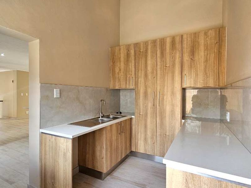 A modern, clean scullery featuring wood-look cabinetry, stone countertops, a stainless steel sink, and neutral tiled flooring with recessed lighting.
