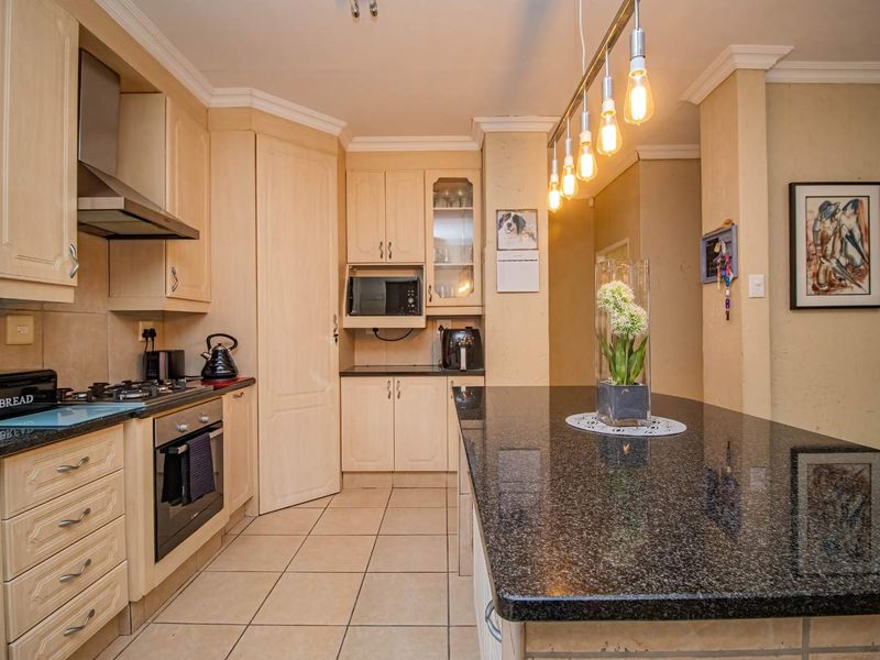 A well-maintained kitchen featuring light wood cabinetry, granite countertops, a central island, and modern built-in appliances with tiled flooring throughout.
