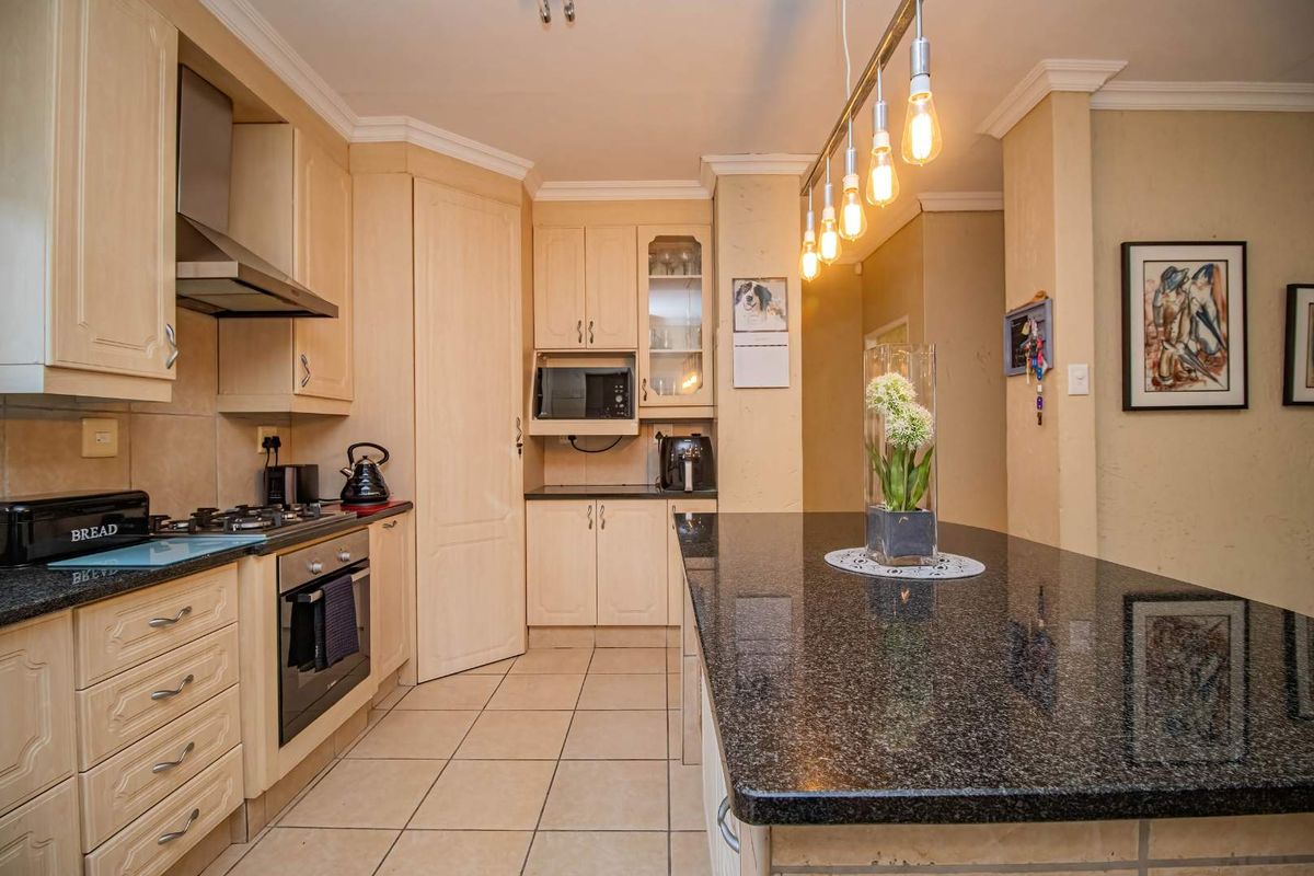 A well-maintained kitchen featuring light wood cabinetry, granite countertops, a central island, and modern built-in appliances with tiled flooring throughout.