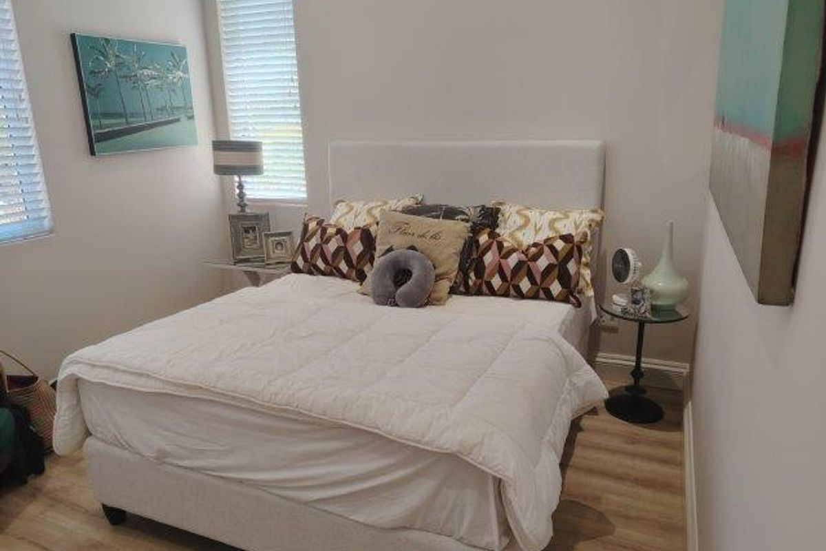 A well-maintained bedroom featuring light-toned laminate flooring and dual windows fitted with venetian blinds, providing a bright and neutral living space.